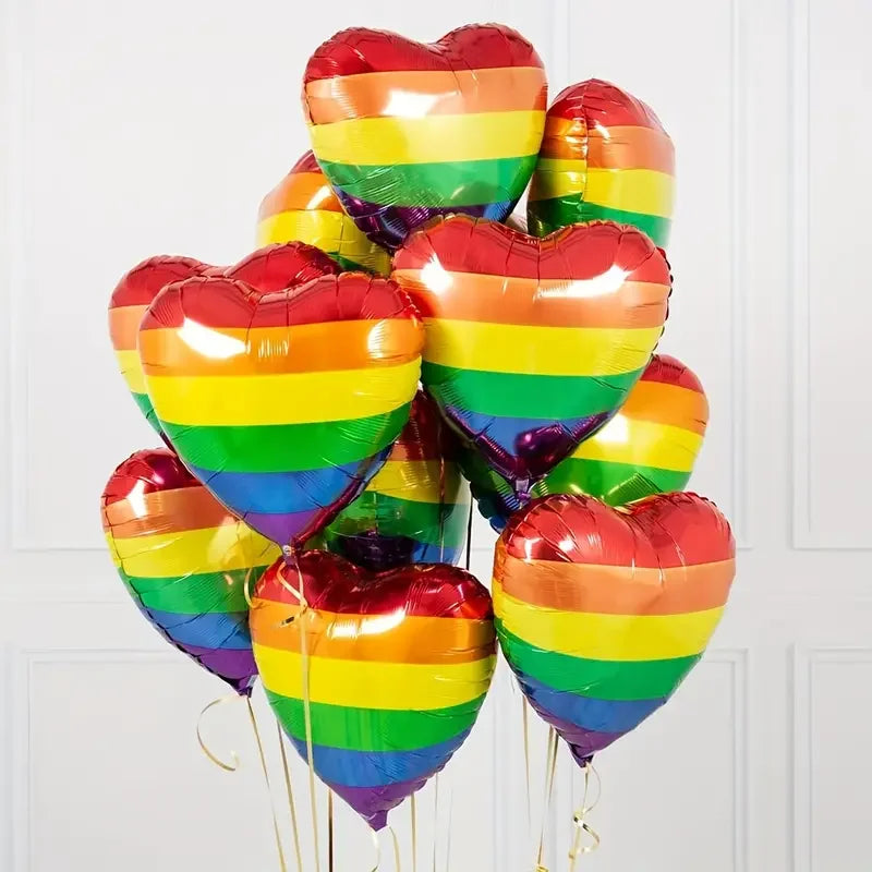 Cluster of rainbow-striped heart-shaped foil balloons against a white paneled wall