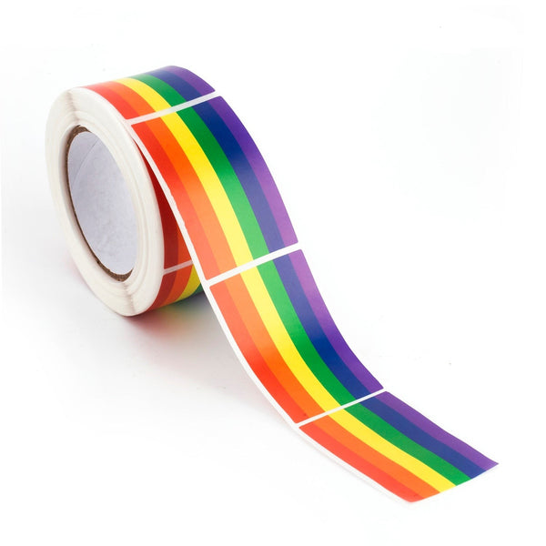 Close-up of a roll of rainbow Pride flag stickers with a strip unspooling across a white surface