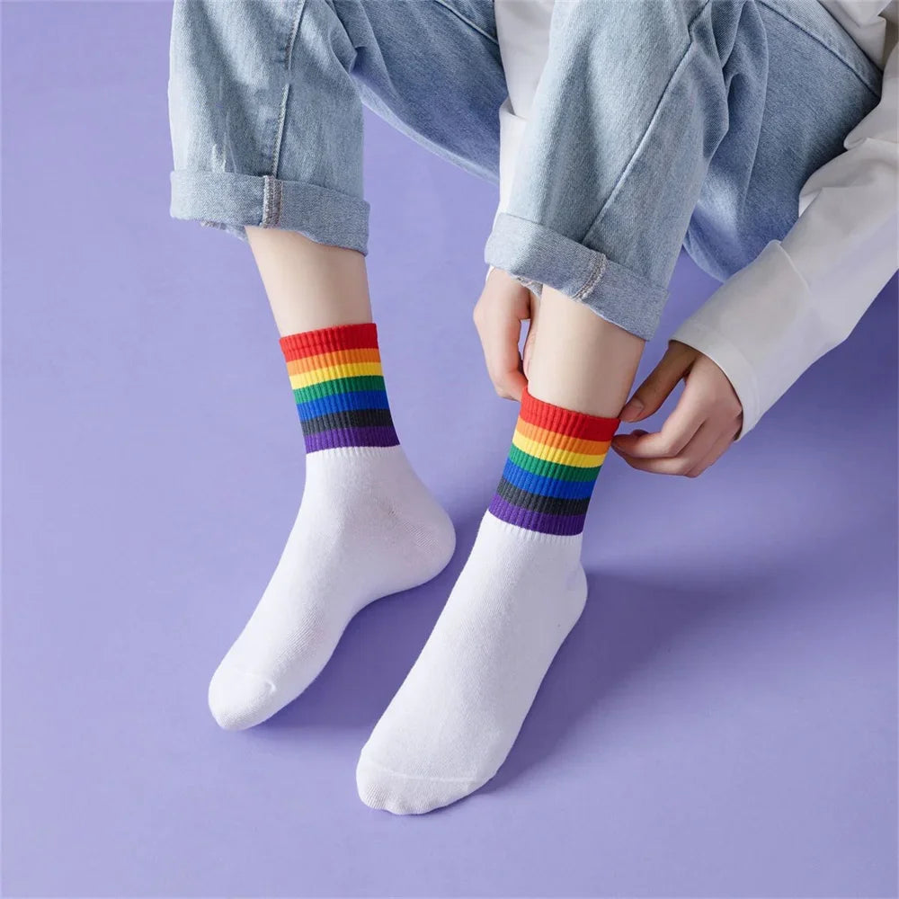 Model wearing white mid-calf socks with rainbow-striped cuffs, adjusting one sock