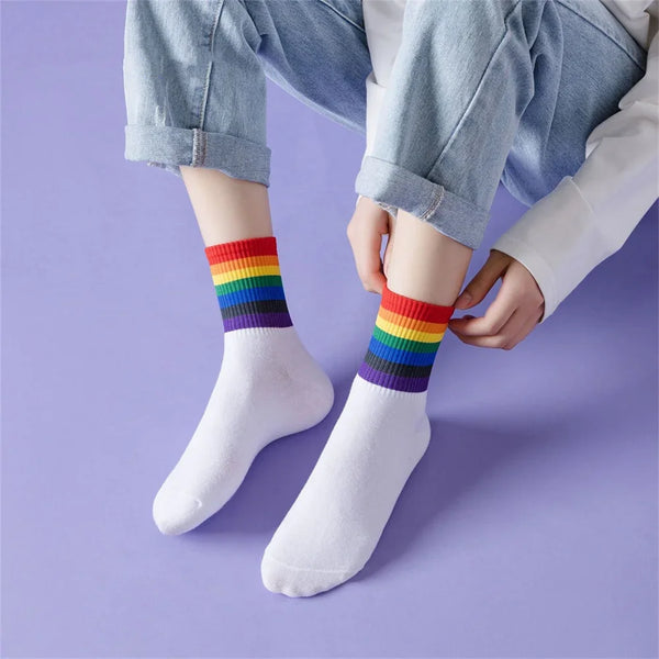 Model wearing white mid-calf socks with rainbow-striped cuffs, adjusting one sock
