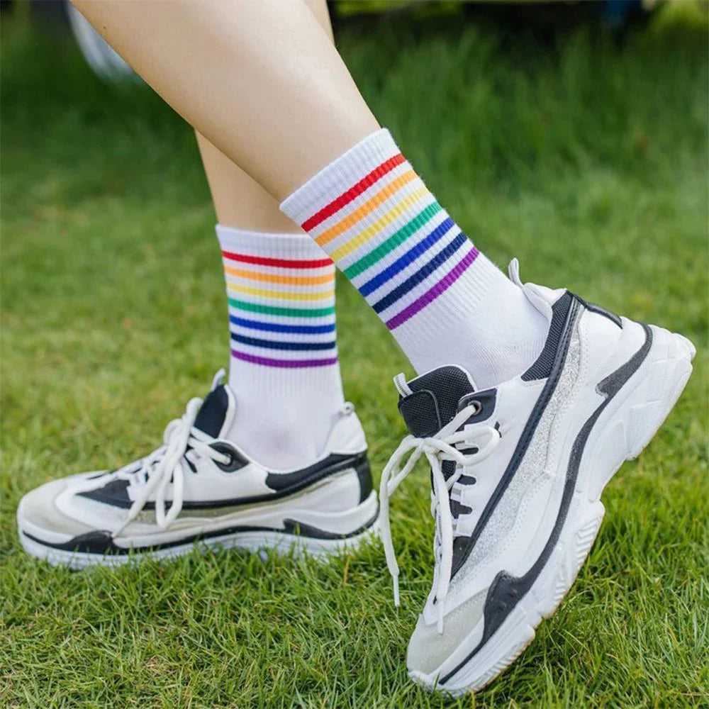 Model wearing white mid-calf rainbow-striped socks with white sneakers on grass
