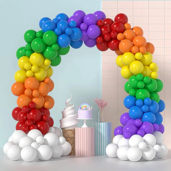 Rainbow balloon arch framing a pastel dessert table with cake and striped containers