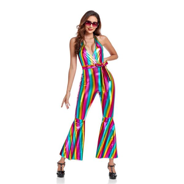 Model in 70s Disco Pride Jumpsuit, featuring a shiny metallic finish with rainbow stripes, halter-neck, deep V-front, matching waist belt, and flared legs, paired with platform heels and sunglasses.