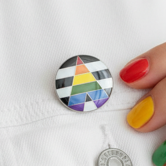 Close-up of the Straight Ally Pride Badge on a white jacket, featuring a rainbow triangle over black and white stripes. A hand with colorful nails adjusts the badge, symbolizing vibrant LGBTQ+ allyship and empowerment.
