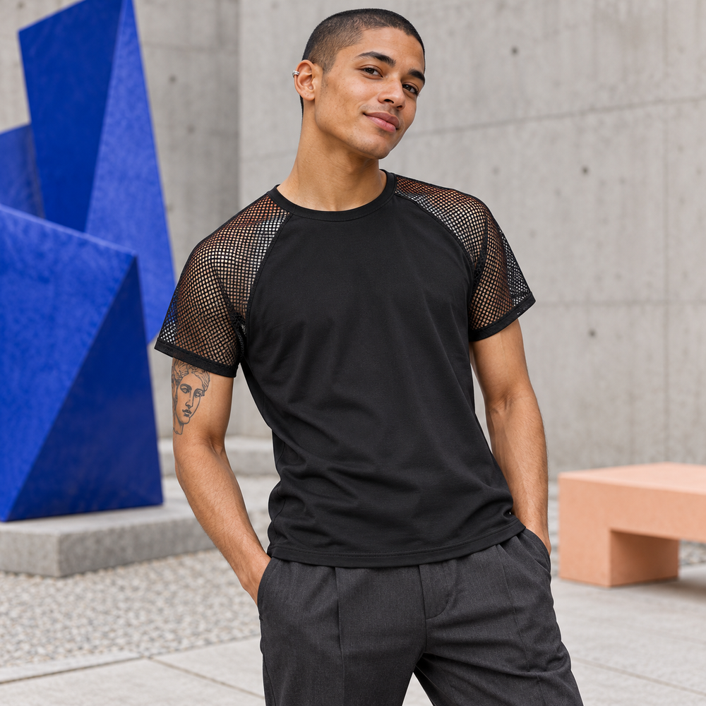 Man wearing a black raglan mesh T-shirt beside a blue wall.