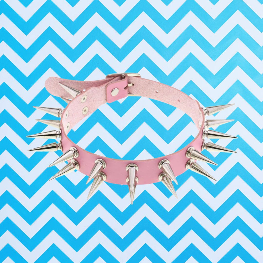 Dark-Femme Edge Goth Choker: Pink leather collar adorned with silver spikes, against a chevron background. A bold, empowering accessory for queer pride and self-expression.