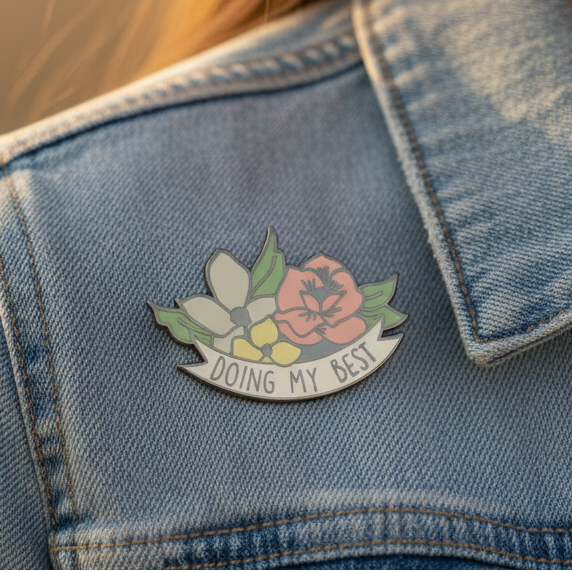 The Doing My Best Enamel Pin features vibrant flowers and a motivational banner, adorning a denim jacket with pride. Perfect for celebrating LGBTQIA+ visibility and self-expression.