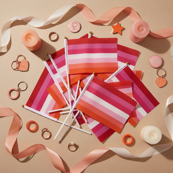 Cluster of 25 Lesbian Handheld Pride Flags styled in a celebratory flat-lay, surrounded by peach and rose-toned accessories, embodying bold queer empowerment and self-expression.