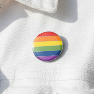 LGBT Pride Badge on white fabric, featuring vibrant six-color rainbow stripes. This empowering accessory showcases bold queer pride with a butterfly button backing, designed for visibility and self-expression.