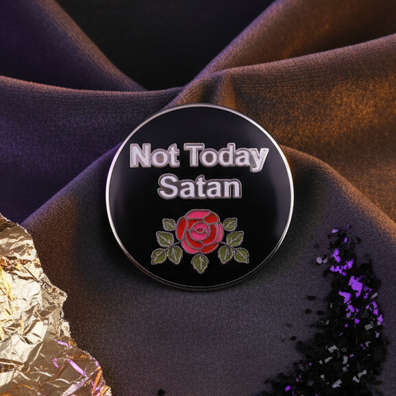 Round black enamel pin reads 'Not Today Satan' with a red rose and green leaves beneath, exuding fierce queer pride, resting on dark purple fabric with glitter embellishments, celebrating bold self-expression.