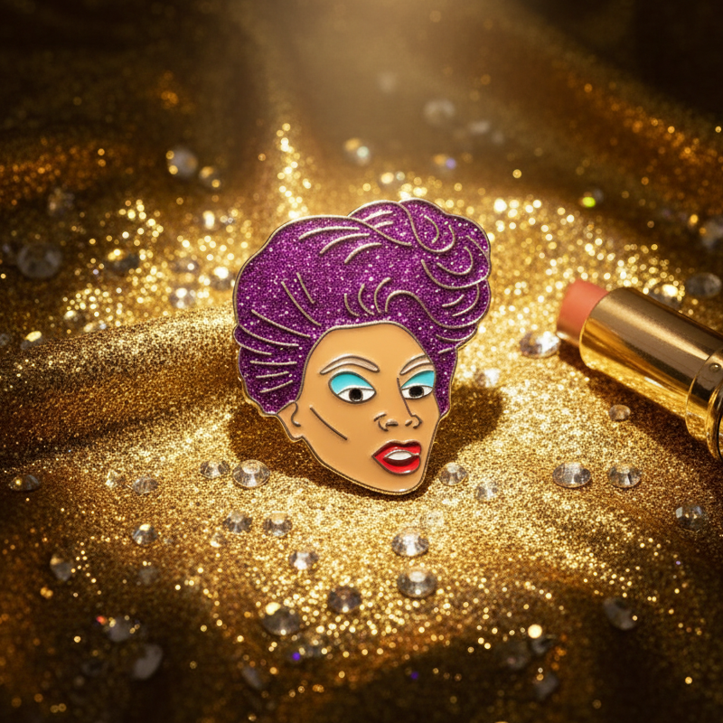Rupaul Enamel Pin featuring bright red lips, turquoise eyeshadow, and glittery purple hair, photographed on sparkling gold fabric with crystal gems. A gold-cased lipstick complements this prideful, empowering accessory.
