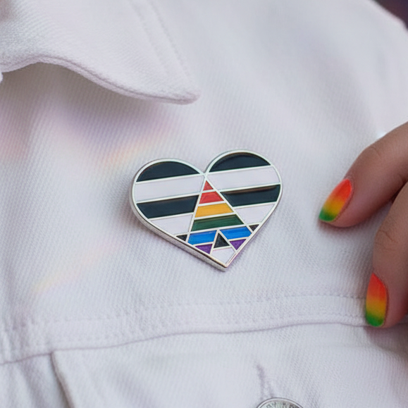 Straight Ally Pride Heart Enamel Pin on a white jacket, featuring black and white stripes with a rainbow A motif. Rainbow-painted nails nearby, showcasing pride, empowerment, and self-expression.