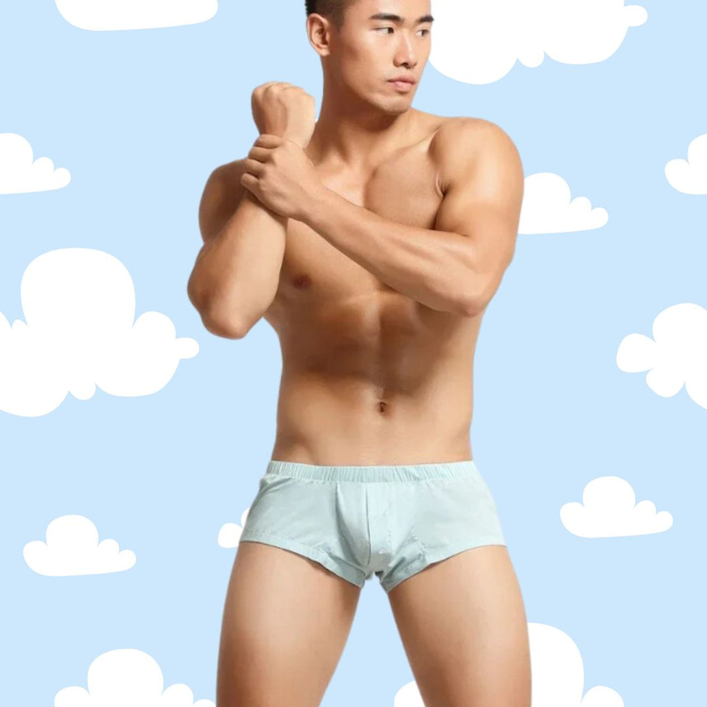 Athletic young man flexing in SEOBEAN Heritage Fit Boxer Shorts, embodying queer pride. Light blue, polyester-spandex blend highlights curves, promoting comfort and confidence. Ideal for bold, self-expressive style.