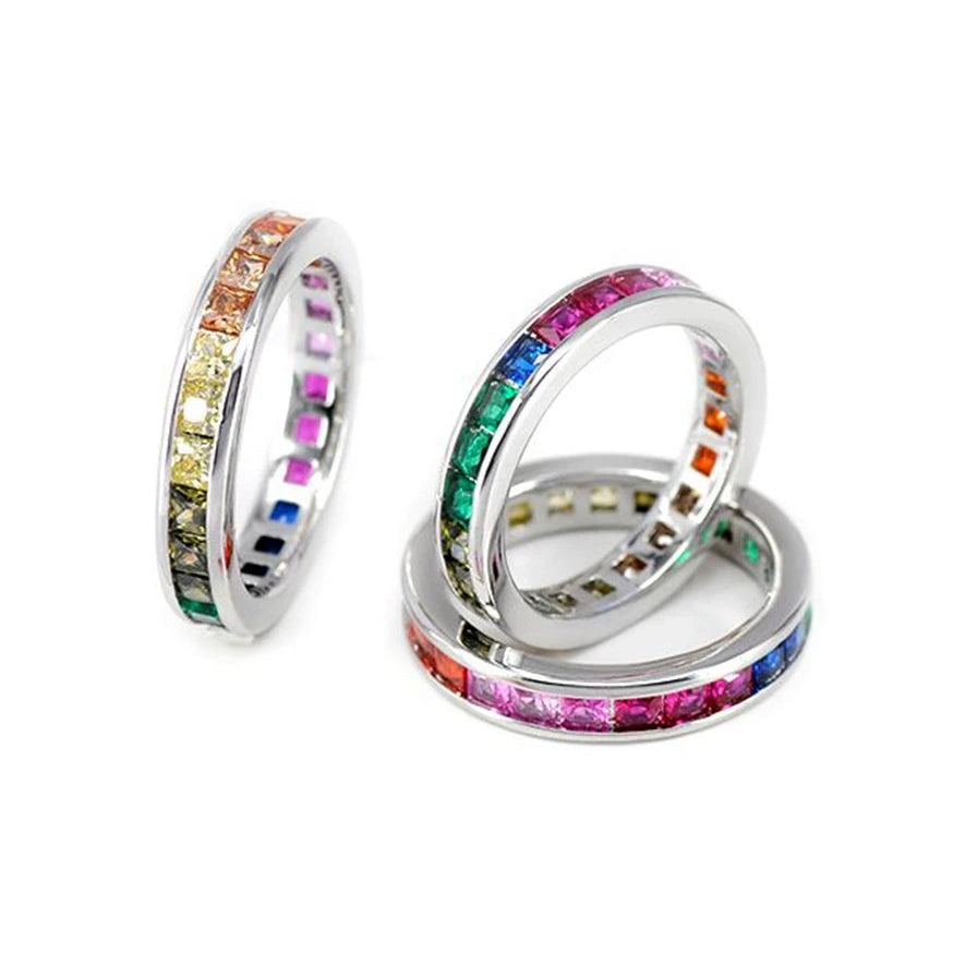 Silver-tone Pride rings with rainbow gemstone rows, stacked and arranged on a white background