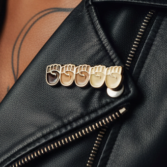 Close-up of a black leather jacket's lapel with five Black Lives Matter Enamel Pins, each a metallic clenched fist, symbolizing solidarity and pride within the vibrant queer community.