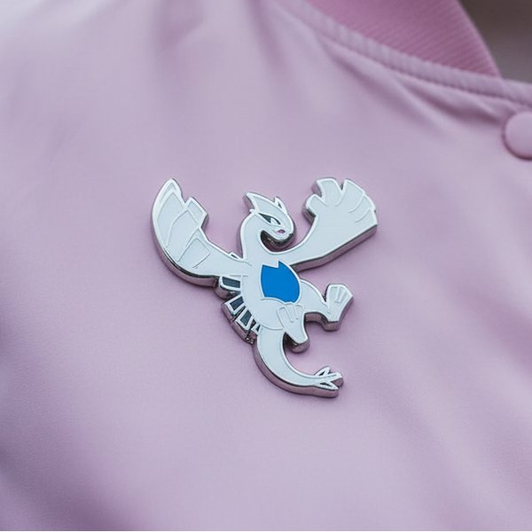 Close-up of a vibrant Lugia Enamel Pin on soft pink fabric, embodying pride and queer self-expression. Perfect for showcasing your fabulous identity with bold, empowering style.