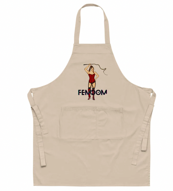 FEMDOM Organic Cotton Apron: Beige apron with a bold illustration of a woman in a red corset, thigh-high boots, and whip, embodying fierce queer pride and empowerment.