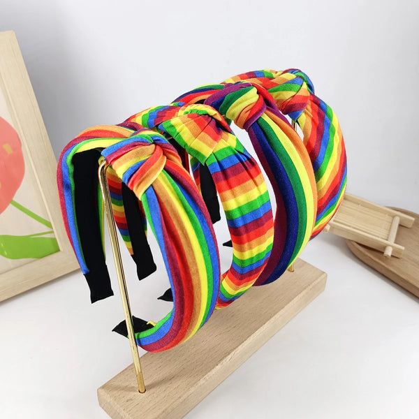 Several rainbow-striped knotted headbands displayed on a wooden stand