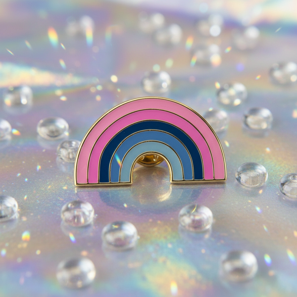 Rainbow arch enamel pin in pink and blue on an iridescent surface with clear droplets