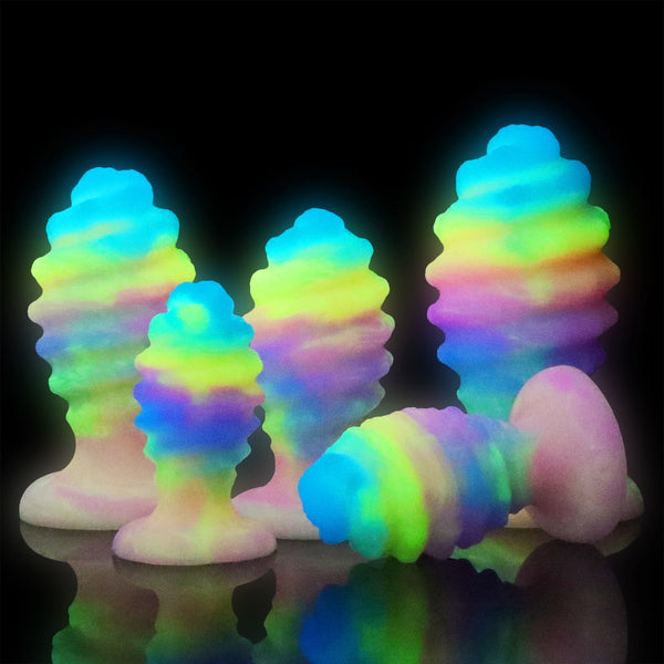 Several glowing rainbow anal plugs with flared bases arranged on a reflective black surface