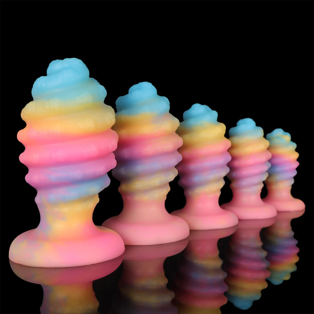 Five pastel rainbow anal plugs arranged by size on a reflective black surface