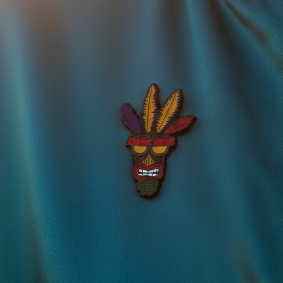 Aku Aku Crash Bandicoot enamel pin with colorful feather headdress on teal fabric