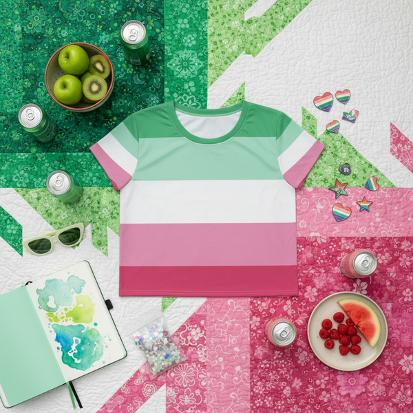 The Abrosexual All-Over Crop T-Shirt, striped and vibrant, lies amid color-coordinated accessories and fruits, showcasing bold, inclusive self-expression and pride. This tight-fitting tee celebrates queer empowerment and individuality.