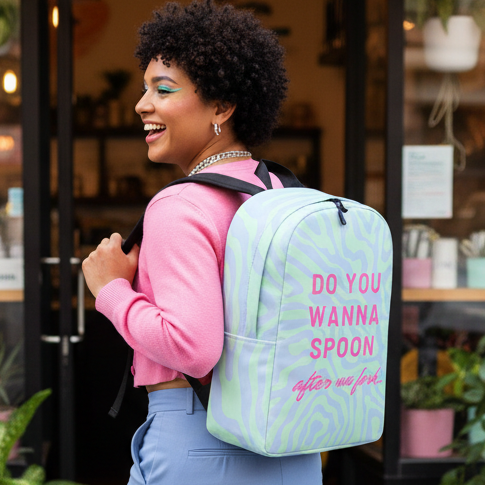 Minimalist backpack reads “Do You Wanna Spoon After We Fork” in bold pink over pastel waves; fab queer style with pink sweater.