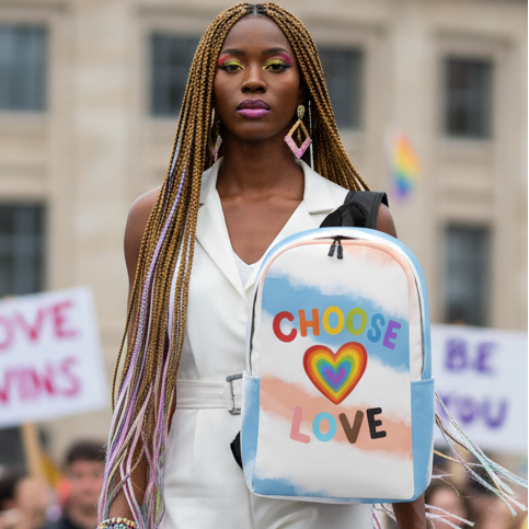 Choose Love Minimalist Backpack with a bold rainbow heart, held by a Black woman in white at Pride; protest signs behind her.