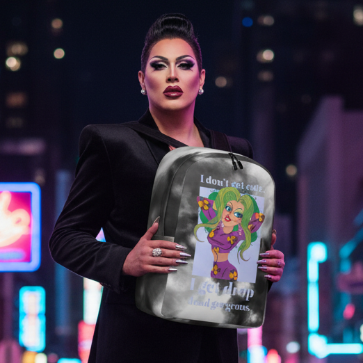 Drop Dead Gorgeous Minimalist Backpack with cartoon print and “I don't get cute, I get drop dead gorgeous,” held by a drag queen in a black blazer at night against neon city lights.
