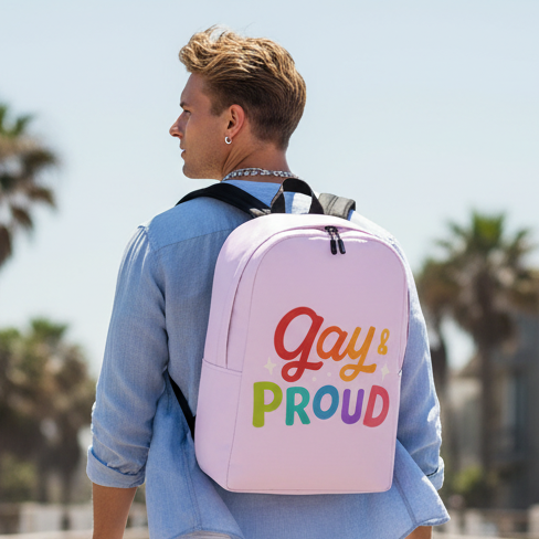 Gay & Proud Minimalist Backpack with bold, colorful "Gay & Proud" slogan, worn by a blond person in a light blue shirt outdoors among palms.