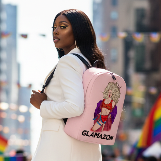 Glamazon Minimalist Backpack with illustrated drag queen and "GLAMAZON" slogan, carried by a femme in a white suit; rainbow flags behind.