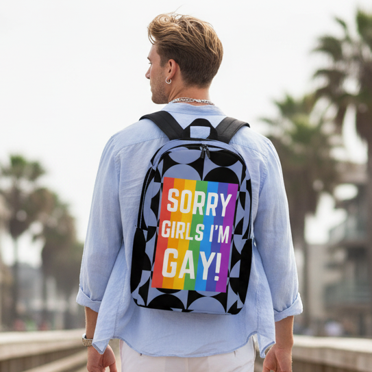 Minimalist backpack with “Sorry Girls I’m Gay!” in bold white text and a rainbow Pride flag, worn by a guy in a light blue shirt.
