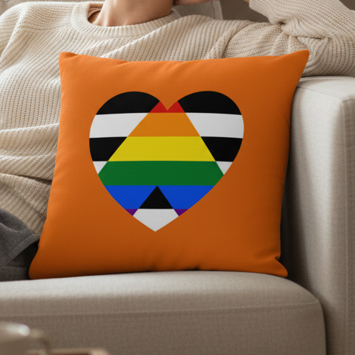 LGBTQ Ally Pillow—heart-shaped, with black and white stripes and a rainbow center—held by someone on a beige sofa.