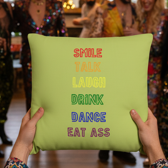 Two hands hold the "Smile, Talk, Laugh, Drink, Dance, Eat Ass" pillow with bold LGBT-themed text; queer party scene behind.