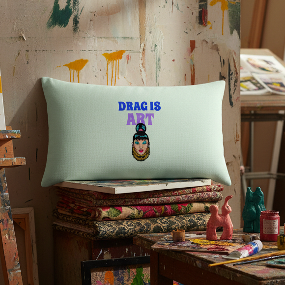 Pale blue "Drag Is Art" pillow with stylized drag queen face, on art books among paint jars and brushes; queer home decor.