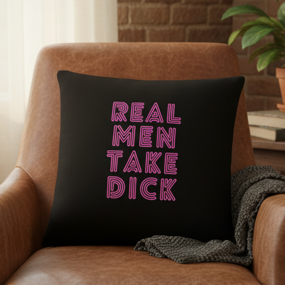 Black pillow with bold pink neon-style text reading "Real Men Take Dick," a queer statement piece for neutral, cozy spaces.