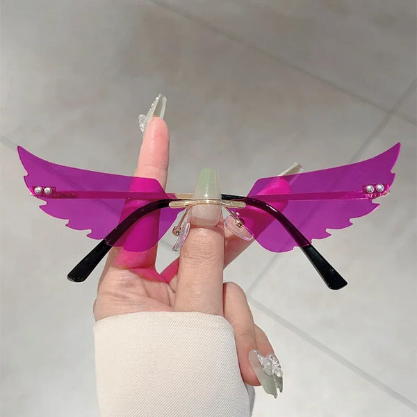 Rear view of magenta wing-shaped sunglasses held by a hand, with rhinestone accents