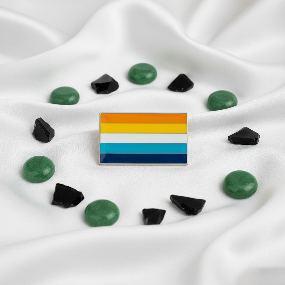 Aroace pride flag enamel pin resting on white satin among green and black stones