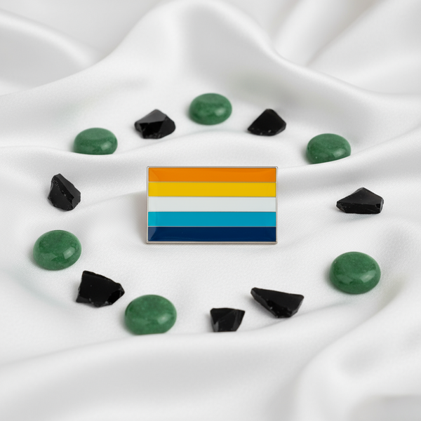 Aroace pride flag enamel pin resting on white satin among green and black stones