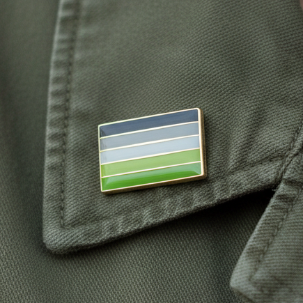 Aromantic Pride Enamel Pin on dark green fabric, featuring gold-bordered horizontal stripes in blues and green