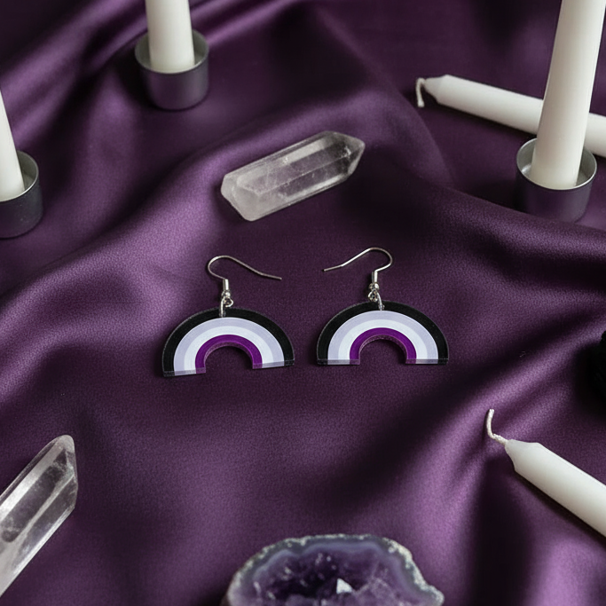 A pair of black, gray, white, and purple rainbow dangle earrings on purple satin