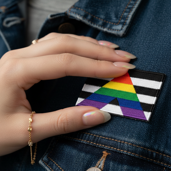 Hand holding a straight ally flag embroidered iron-on patch against a denim jacket