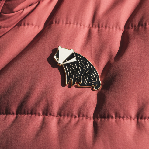 Badger Enamel Pin styled on a pink quilted jacket, celebrating fierce queer pride and self-expression with bold design.