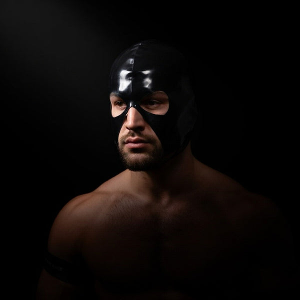 Person wearing a glossy black full-face mask with eye openings against a dark background