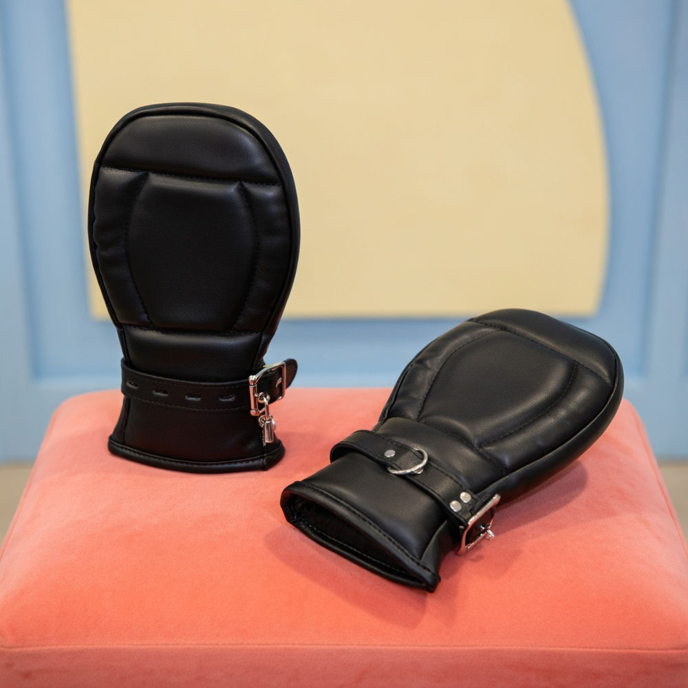 Pair of black padded pup mitt cuffs with buckles displayed on a coral cushion.