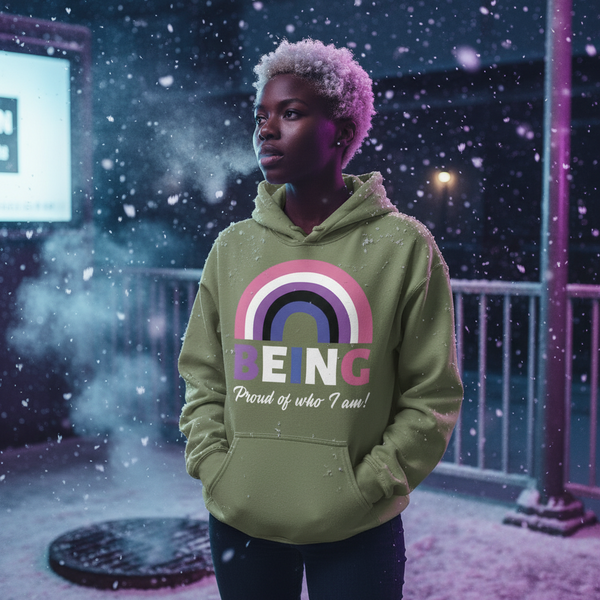 Person wearing an olive hoodie with a rainbow graphic and “BEING Proud of who I am!” text in falling snow