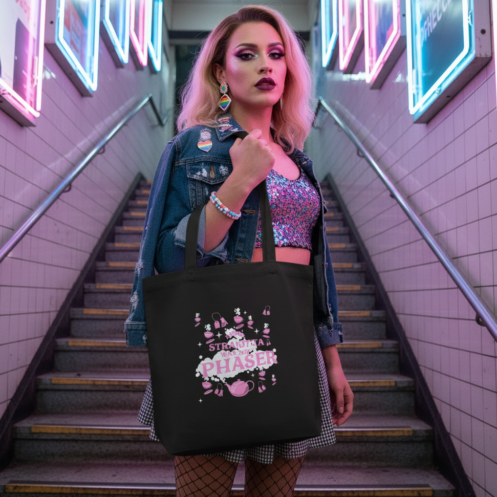 Person models a black tote reading “STRAIGHT WAS MY PHASE” on a neon-lit subway staircase
