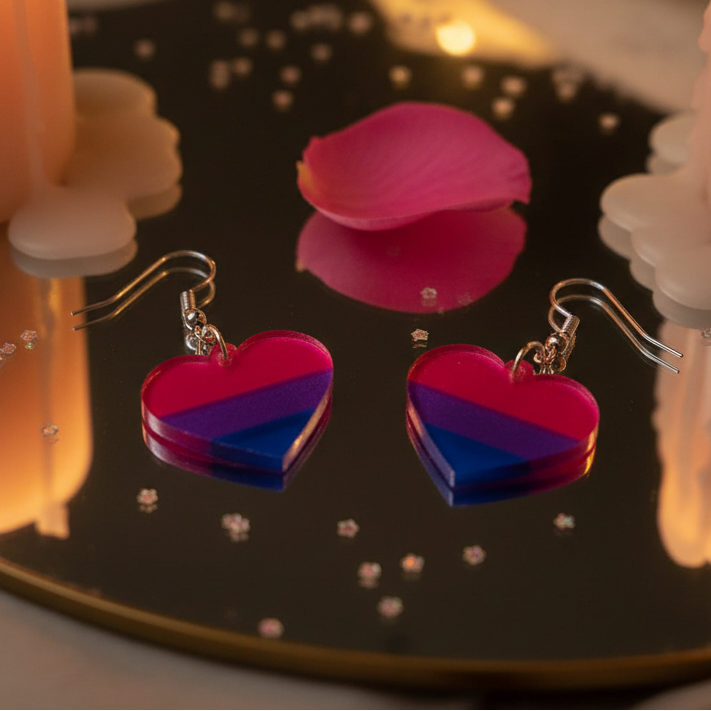 Pair of pink, purple, and blue striped heart dangle earrings on a reflective tray