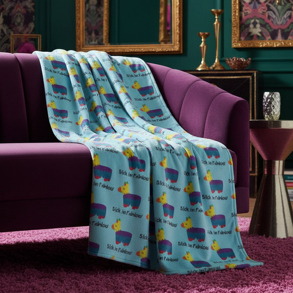 “Bitch I'm Fabulous!” light blue throw blanket with colorful llamas draped on a purple velvet sofa, pink rug, gold accents